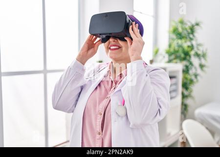 Young beautiful plus size woman doctor using virtual reality glasses at clinic Stock Photo