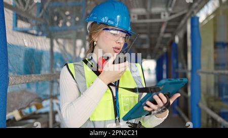 Young blonde woman architect talking on walkie-talkie using touchpad at street Stock Photo