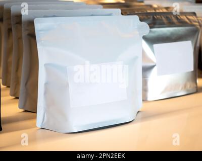Close Up empty blank white label on modern white and silver foil bags coffee beans packaging. Mockup template sticker label. Row of paper zipper pouch Stock Photo