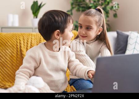 Adorable boy and girl using laptop sitting on sofa at home Stock Photo