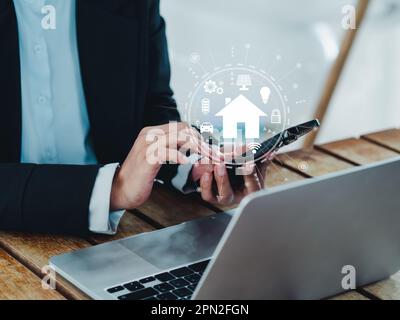 Smart home technology concept. Virtual screen of futuristic smart home digital management icons and symbols on smart mobile phone holding by businessm Stock Photo