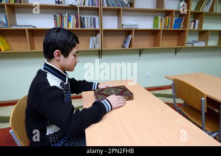 Classroom of the medrese. Muslim boy sitting at a school desk, Quran placed in front of him. October 21, 2018. Islamic culture centre, Kiev, Ukraine Stock Photo