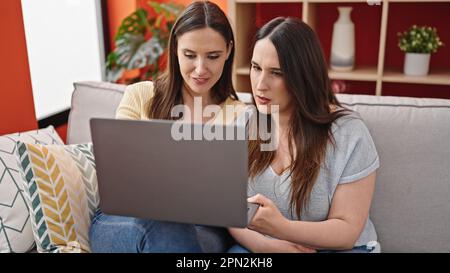 Two women sitting on sofa using laptop at home Stock Photo