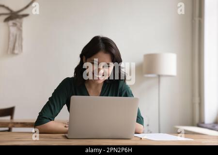 Happy Armenian female freelance doing telework using laptop Stock Photo