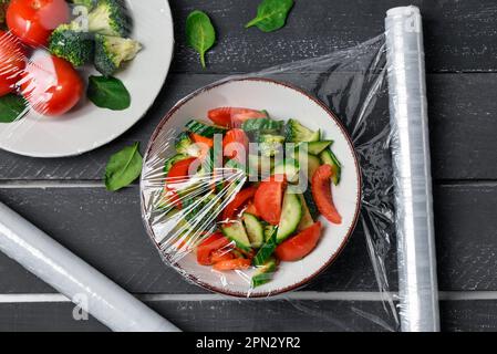 Bowl with salad wrapped with stretch wrap on dark wooden background Stock Photo