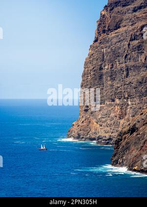 A pirate sailboat sets out on an adventure amidst the awe-inspiring cliffs of Los Gigantes, with the vast Atlantic Ocean stretching into the distance. Stock Photo