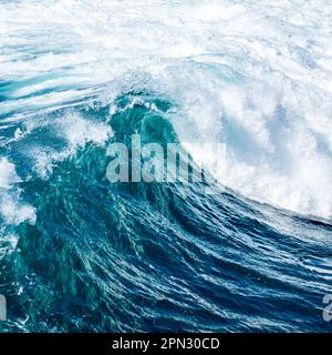 Side view of a wave crashing with great force, producing a magnificent display of white foam and turbulent blue waters, showing nature's raw power. Stock Photo