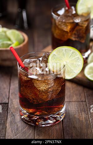 Rum and cola cocktail with lime slice on rustic wooden table Stock Photo