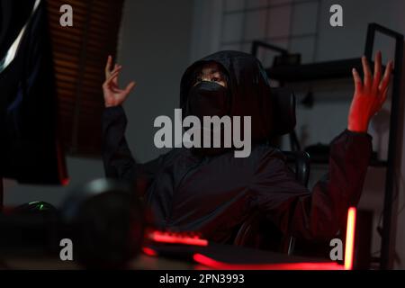 Hacker in hoodie raising hands while having problem with hacking programming system or server. Stock Photo