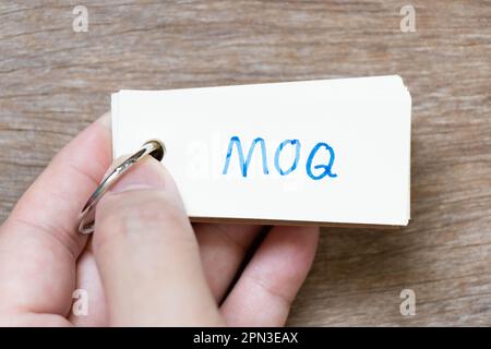 Hand hold flash card with handwriting in word MOQ (Abbreviation of Minimum Order Quantity) on wood background Stock Photo