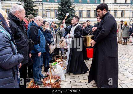 A priest blesses Easter food with Holy Water as Ukrainian believers attend the Easter Sunday traditional celebration in St. Michael's Golden-Domed Monastery in central Kyiv, the capital of Ukraine on April 16, 2023. According to the tradition the faithful bring their Easter food in a basket to be purified, it always is Pasha (Easter bread), painted egg (pysanka) among other. Most of Ukrainians are Orthodox Christians or Greek Catholic Christians, both observe the eastern rite of Easter. Kyiv remains relatively peaceful as the Russian invasion continuous and Ukraine prepares for a spring counte Stock Photo