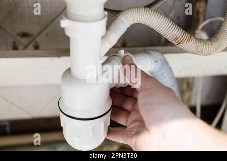 plumber mounts old plastic siphon close-up in kitchen of village house to clean drain Stock Photo