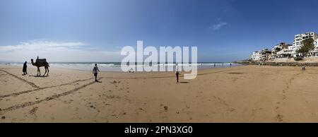 Morocco, Africa: panoramic view of a camel and boys playing soccer on the beach of Taghazout, small berber fishing village near Agadir Stock Photo