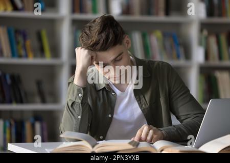 Student guy studying in library feels bored or tired Stock Photo