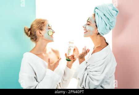 Own spa salon at home. Conception of skin care by using white mask and cucumbers on the face. Two female sisters have weekend. Stock Photo