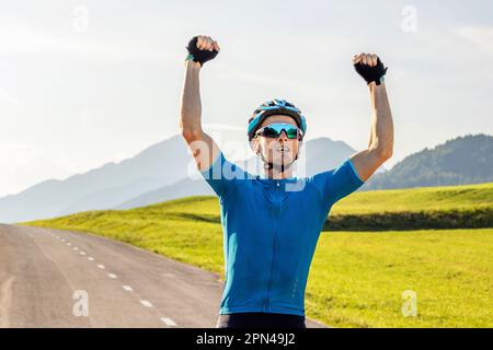 Male athlete professional racing cyclist riding a bike with arms raised above the head, in a victory pose Stock Photo