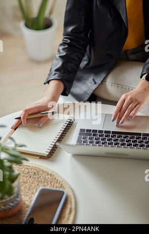 Close up woman hand using laptop and making notes in notebook sitting at workplace at home, remote work Stock Photo