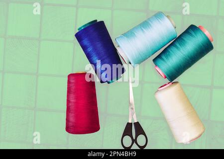 Multi colored threads and tailor scissors on a wooden green plaid surface Stock Photo