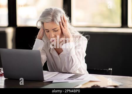 Mature Businesswoman Suffering From Headache Pain At Laptop In Office Stock Photo