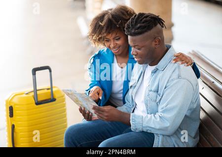 Black Spouses Checking Travel Route With Map While Sitting At Railway Station Stock Photo