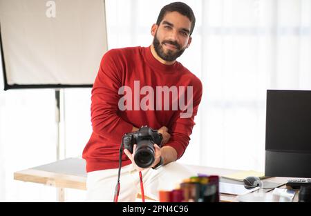 Positive young guy professional photographer posing at his workplace Stock Photo