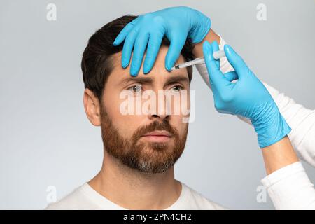 Handsome middle aged bearded man getting brow lift, beautician in gloves making beauty injection for handsome male Stock Photo