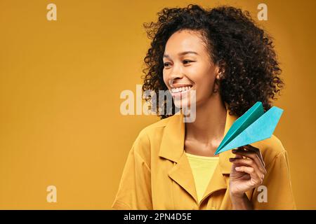 African American female tourist throws paper airplane simulating air traveling, dreaming about trip with happy toothy smile Stock Photo