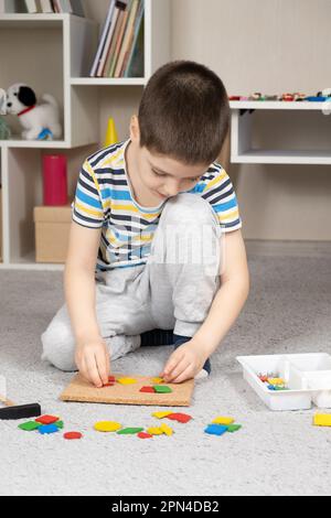 A 5-year-old boy creates a picture from multi-colored pieces of a mosaic on a blackboard. Stock Photo