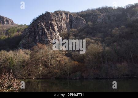 Sun shining on a rock formation in Rotenfels on a hill with trees above the Nahe River on a winter day in Germany. Stock Photo