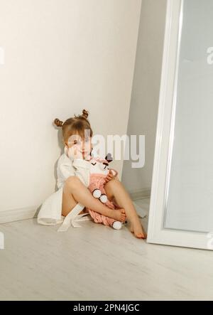 A girl in a bathrobe plays on the floor with a knitted unicorn. Stock Photo