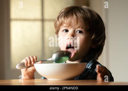 Young kid sitting on the table eating with funny expression on face. Tasty kids breakfast. Tasty kids breakfast. Cheerful baby child eats food itself Stock Photo