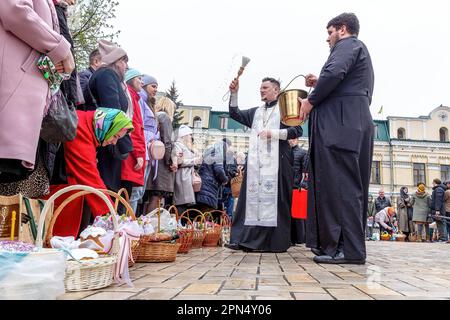 A priest blesses Easter food with Holy Water as Ukrainian believers attend the Easter Sunday traditional celebration at St. Michael's Golden-Domed Monastery in central Kyiv. According to the tradition the faithful bring their Easter food in a basket to be purified, it is always Pasha (Easter bread), painted egg (pysanka) among other. Most of Ukrainians are Orthodox Christians or Greek Catholic Christians, both observe the eastern rite of Easter. Kyiv remains relatively peaceful as the Russian invasion continuous and Ukraine prepares for a spring counter-offensive to retake Ukrainian land occup Stock Photo