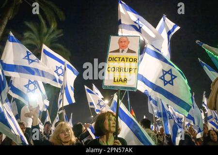 Netanya, Israel. 15th Apr, 2023. Anti-reform protestors hold Israeli flags and a sign with Prime Minister Benjamin Netanyahuís photo, the sign reads ìdictator, corrupt, liarî during a demonstration. Hundreds and thousands of people rallied for the 15th straight week Saturday against Netanyahu's coalition judicial overhaul plans, a day after leading ratings agency Moody's downgraded Israel's economic outlook from positive to stable amid the coalition's highly controversial proposals to shackle the judiciary. Credit: SOPA Images Limited/Alamy Live News Stock Photo