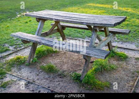 Old rustic wooden picnic table in outdoor park picnic area with green grass and gravel underneath.  Stock Photo