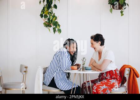 Happy friends laughing together in coffee shop. Two female friends having a good conversation at a modern coffee shop Stock Photo