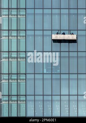 A glass building wall with window washers descending the facade on a lift platform in Tokyo, Japan Stock Photo