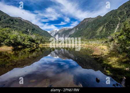 Mountain and sky reflections on the surface of small Peters Pool in Franz Josef Stock Photo