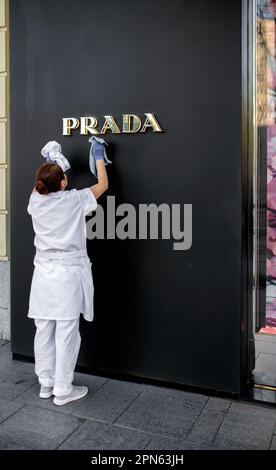 Cleaning services. A cleaning lady cleans the window of a Prada store. A woman washes the facade of a building with a wet rag. Cleaning services - wor Stock Photo