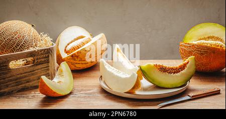 Various sliced melons on wooden table by stone wall Stock Photo