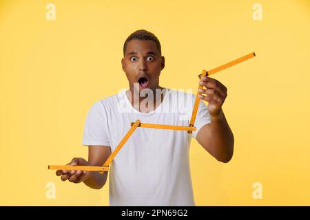 Concept of income growth, amazed African American man holding folding ruler and showing growth chart on the stock exchange. Man is standing on bright yellow background with copy space for designers to add their own text or graphics. High quality photo Stock Photo