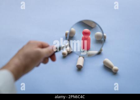 Magnifying glass on red wooden doll with other fallen dolls by the side, Talent search or selection concept. Stock Photo
