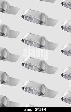 Coffee bags regular pattern. Blank white foil pouch on grey background in minimal style with natural harsh shadows. Monochrome food photo. Packaging t Stock Photo