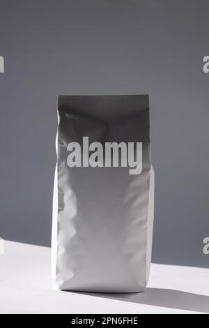 Blank foil food or drink bag on white background in minimal style with natural light shadow. Monochrome photo. Packaging with valve and seal template Stock Photo