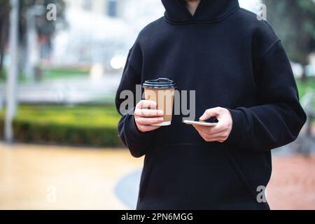 Man holding paper cup and smartphone outdoors. Stock Photo