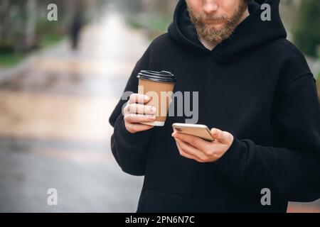 Man holding paper cup and smartphone outdoors. Stock Photo