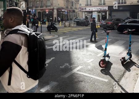 Predestrians walk by Rental e-scooters parked on the road in a designated parking area painted on the ground, in Paris, France. Stock Photo