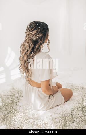 Young woman with flowers in hair sitting by baby's-breath flowers Stock Photo