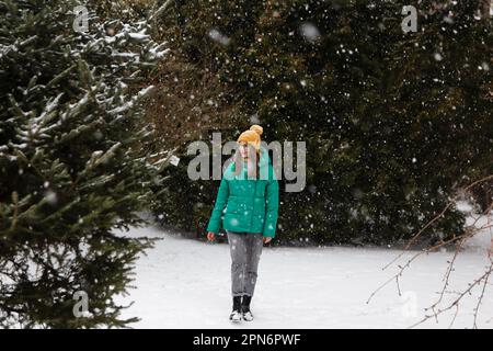 woman in yellow hat, glasses and green jacket walks in park in winter Stock Photo