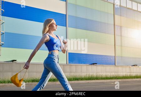 Young blond woman wearing blue jeans and top walking in the city Stock Photo