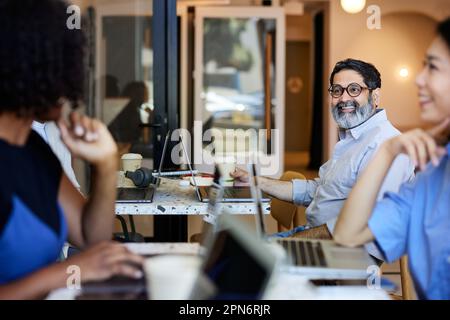 Happy mature businessman discussing with colleagues sitting in cafe Stock Photo